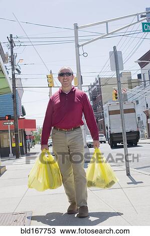 Stock Image - Hispanic man carrying shopping bags on city sidewalk. Fotosearch