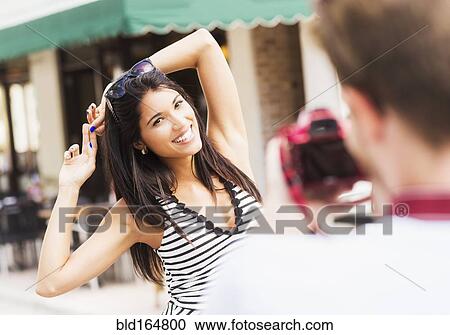 Stock Image - Hispanic man photographing girlfriend outdoors. Fotosearch
