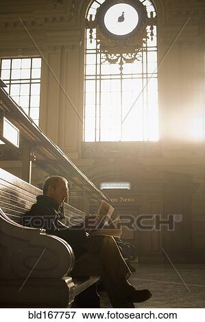 Stock Photo - Hispanic man reading newspaper in train station. Fotosearch