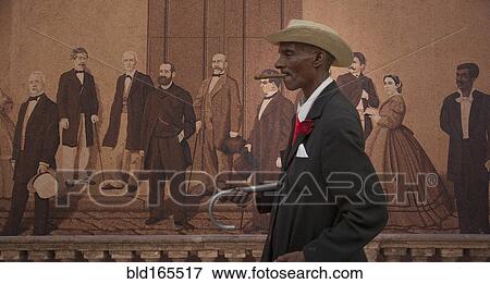 Stock Photo - Hispanic man walking past mural, Havana, Cuba. Fotosearch