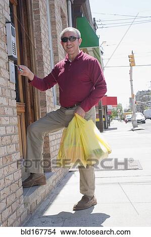 Picture - Hispanic man with shopping bags unlocking front door. Fotosearch