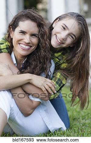 Stock Image - Hispanic mother and daughter hugging in backyard. Fotosearch