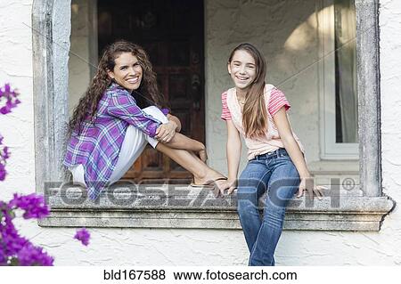 Stock Photo - Hispanic mother and daughter sitting in window sill outdoors. Fotosearch