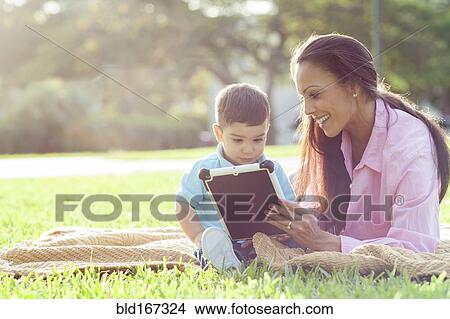 Picture - Hispanic mother and son reading in park. Fotosearch
