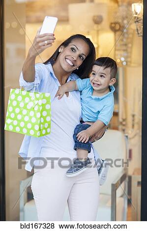 Stock Photo - Hispanic mother and son taking selfies and shopping. Fotosearch