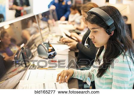 Stock Photo - Hispanic student listening to headset at desk. Fotosearch