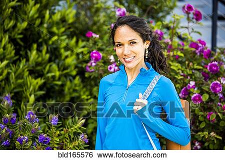 Stock Photograph - Hispanic woman carrying yoga mat in garden. Fotosearch