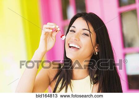 Stock Image - Hispanic woman eating cherry outdoors. Fotosearch