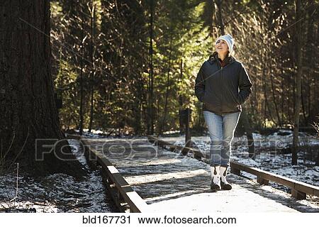 Stock Image - Hispanic woman on wooden walkway in snowy forest. Fotosearch
