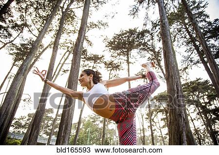 Stock Image - Hispanic woman practicing yoga in forest. Fotosearch