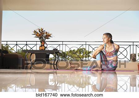 Stock Image - Hispanic woman practicing yoga on balcony. Fotosearch