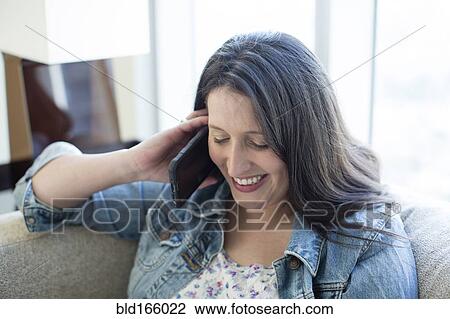 Stock Image - Hispanic woman talking on cell phone on sofa. Fotosearch