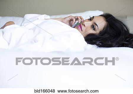 Stock Photo - Hispanic woman talking on cell phone on bed. Fotosearch