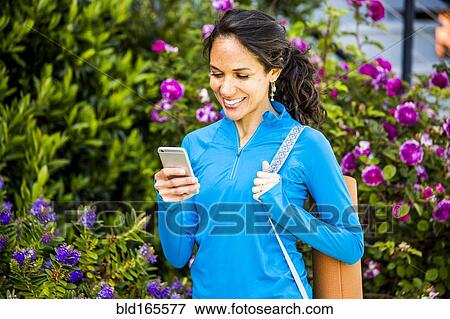 Stock Photo - Hispanic woman using cell phone in garden. Fotosearch
