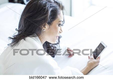 Stock Photo - Hispanic woman using cell phone on bed. Fotosearch