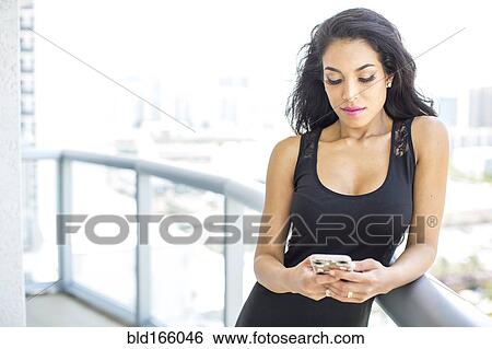 Stock Photograph - Hispanic woman using cell phone on balcony. Fotosearch