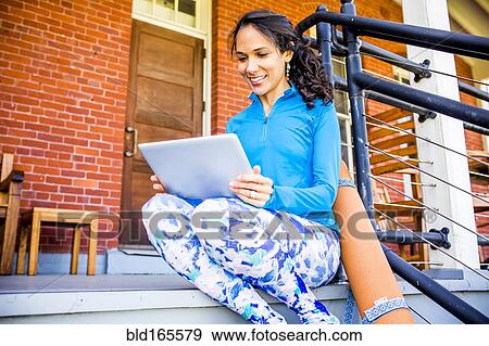 Stock Photo - Hispanic woman using digital tablet on porch. Fotosearch