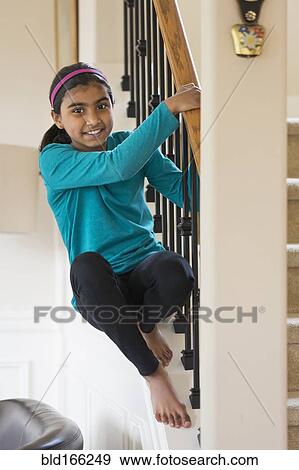 Stock Photo - Indian girl climbing on staircase banister. Fotosearch