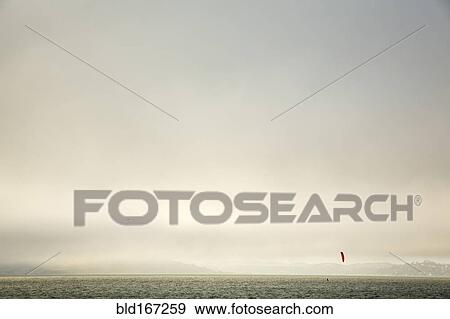 Stock Photo - Kiteboarder on ocean under cloudy sky. Fotosearch