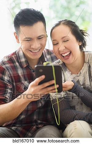 Stock Image - Laughing couple watching digital tablet on sofa. Fotosearch