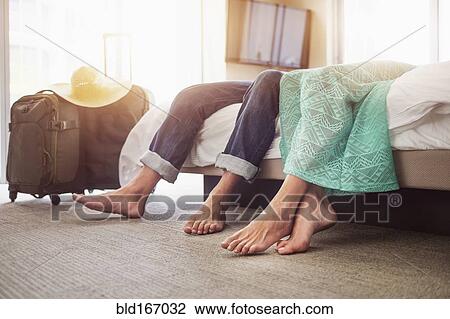 Stock Image - Legs of couple laying on bed in hotel room. Fotosearch