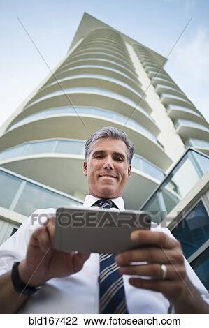 Stock Image - Low angle view of Caucasian businessman using cell phone at high rise building. Fotosearch