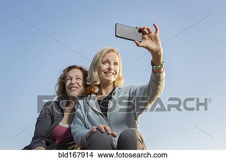 Low angle view of Caucasian women taking selfie View Large Photo Image Picture - Low angle view of Caucasian women taking selfie. Fotosearch