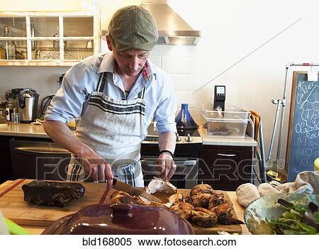 Stock Photography - Man carving roasted meat in kitchen. Fotosearch