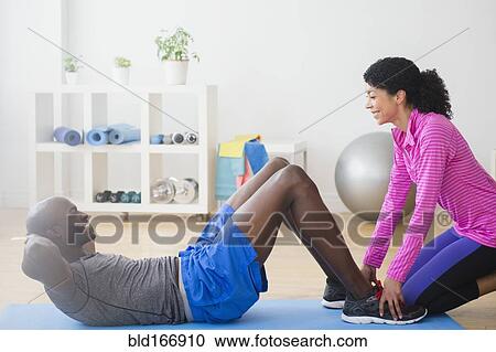 Stock Image - Man doing sit-ups with trainer in gym. Fotosearch