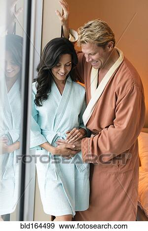 Stock Photo - Man rubbing belly of pregnant wife in bedroom. Fotosearch