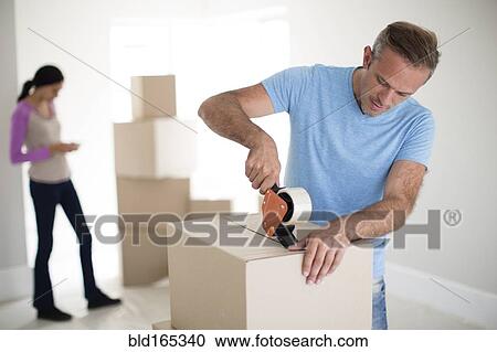 Stock Image - Man taping cardboard box to move. Fotosearch