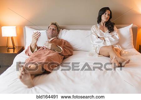 Stock Image - Man with digital tablet ignoring girlfriend in bed. Fotosearch