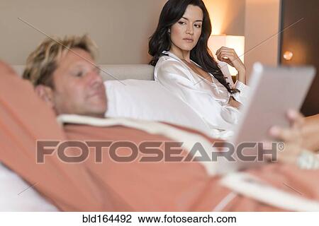 Stock Image - Man with digital tablet ignoring girlfriend in bed. Fotosearch