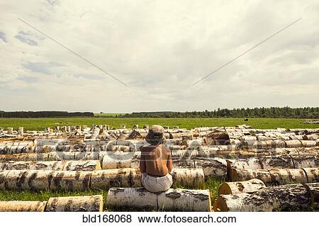 Mari boy sitting on log in rural field View Large Photo Image Stock Photo - Mari boy sitting on log in rural field. Fotosearch