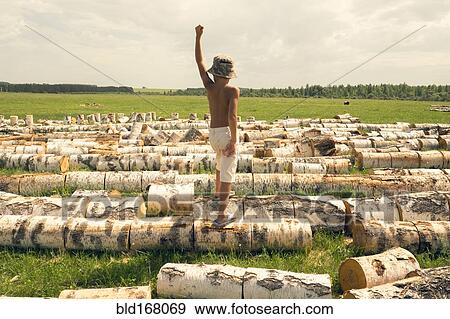 Stock Photo - Mari boy standing on logs in rural field. Fotosearch