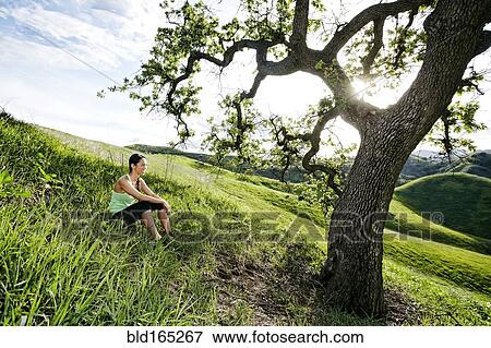 Stock Photo - Mixed race athlete sitting on rural hillside. Fotosearch