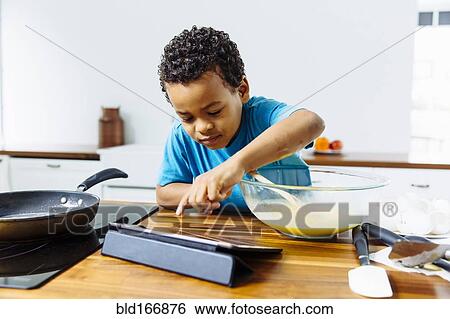 Stock Photograph - Mixed race boy cooking breakfast with digital tablet in kitchen. Fotosearch