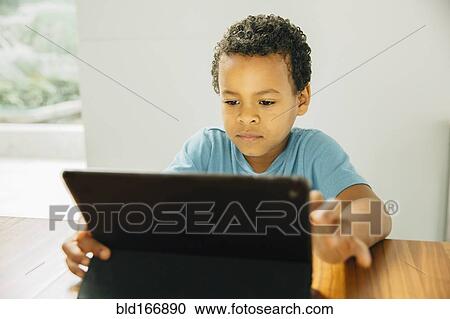 Stock Image - Mixed race boy using digital tablet at table. Fotosearch