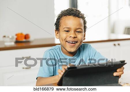 Stock Photo - Mixed race boy using digital tablet in kitchen. Fotosearch