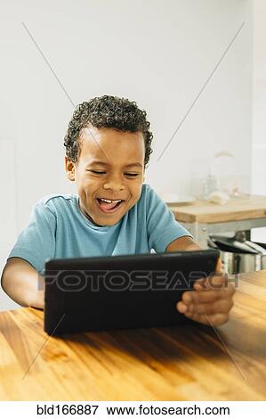 Stock Photo - Mixed race boy using digital tablet in kitchen. Fotosearch