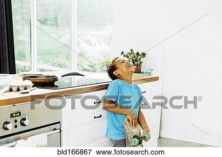 Stock Photo - Mixed race boy with skateboard laughing in kitchen. Fotosearch