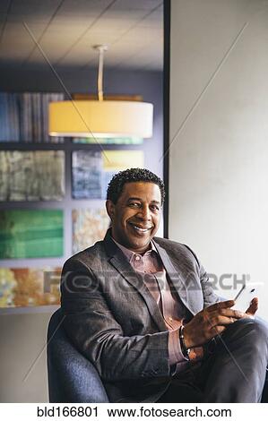 Stock Image - Mixed race businessman using cell phone in office lobby. Fotosearch