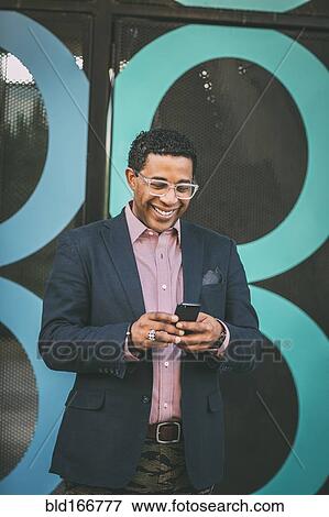 Stock Photo - Mixed race businessman using cell phone outdoors. Fotosearch
