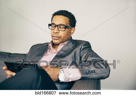 Mixed race businessman using digital tablet on sofa View Large Photo Image Stock Photo - Mixed race businessman using digital tablet on sofa. Fotosearch