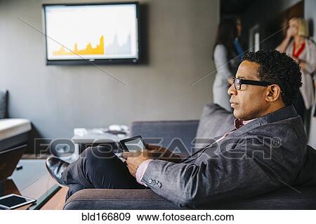 Stock Photo - Mixed race businessman using digital tablet in office lounge. Fotosearch