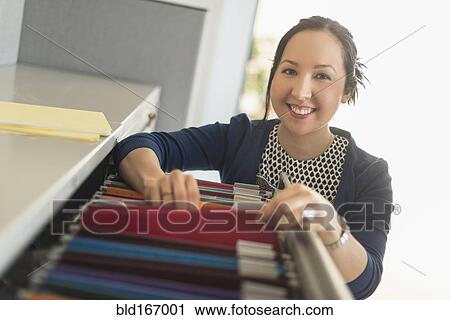 Stock Image - Mixed race businesswoman choosing files in office. Fotosearch