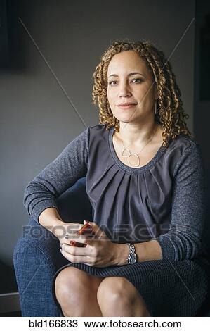 Stock Image - Mixed race businesswoman smiling in armchair. Fotosearch