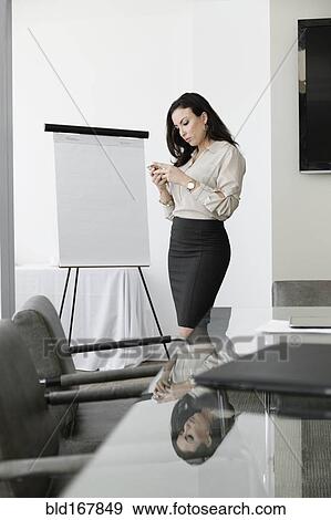 Stock Photo - Mixed race businesswoman using cell phone in conference room. Fotosearch