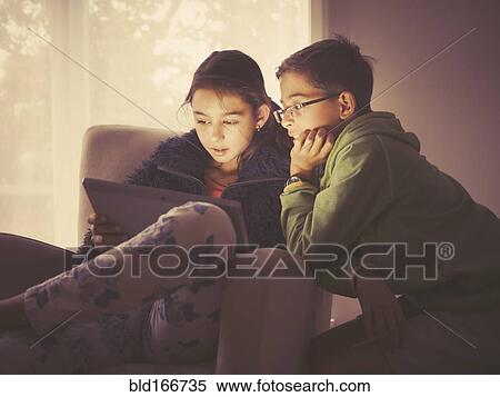 Stock Photography - Mixed race children using digital tablet in living room. Fotosearch