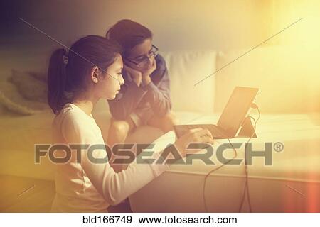 Stock Photo - Mixed race children using laptop on sofa. Fotosearch